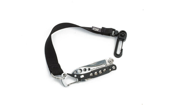 An 8-inch Black Key Strap with a snaphook at one end and a split-ring o-ring at the other with a pocket knife fed through the split-ring o-ring.
